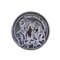 A round silver-toned coin or medallion engraved with a couple embracing and the text 'Happy Raksha Bandhan' around the border, shown on a plain white background.