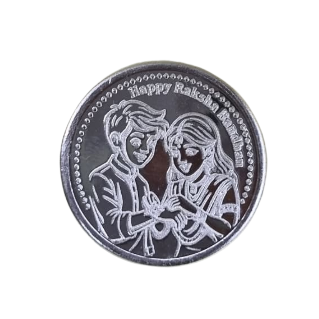 A round silver-toned coin or medallion engraved with a couple embracing and the text 'Happy Raksha Bandhan' around the border, shown on a plain white background.